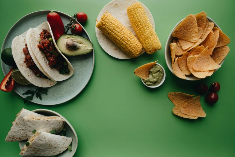 a green table topped with plates of food, by Carey Morris, pexels, corn, taco, background image, crisps