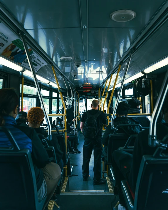 a group of people sitting on a bus, back facing the camera, man standing, trans rights, thumbnail