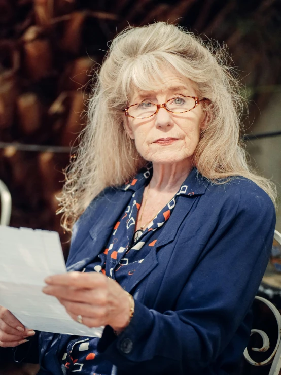 a woman sitting at a table reading a piece of paper, photorealism, with glasses on, gandalf as a woman, jenny savile, promo image