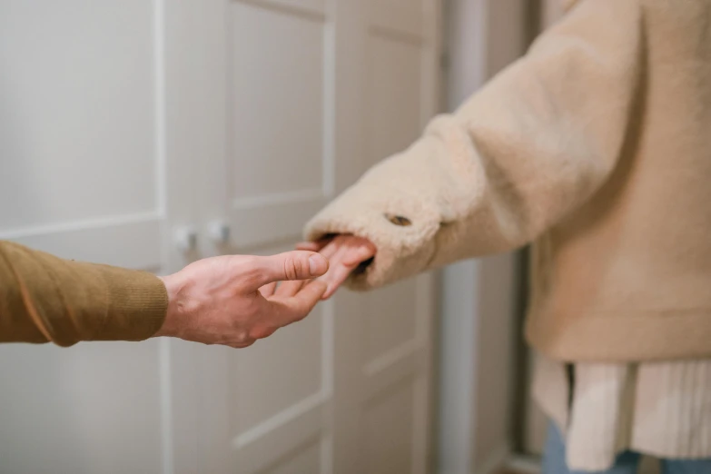 a man and a woman holding hands in front of a door, by Emma Andijewska, trending on pexels, light brown coat, hands on counter, woman holding another woman, thumbnail