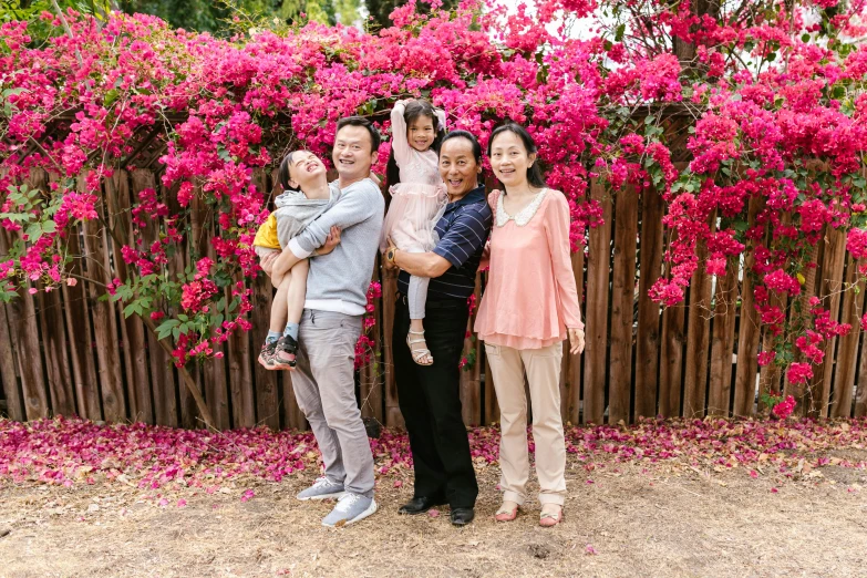 a family poses for a picture in front of pink flowers, a portrait, shin hanga, bougainvillea, avatar image, louise zhang, professional photo