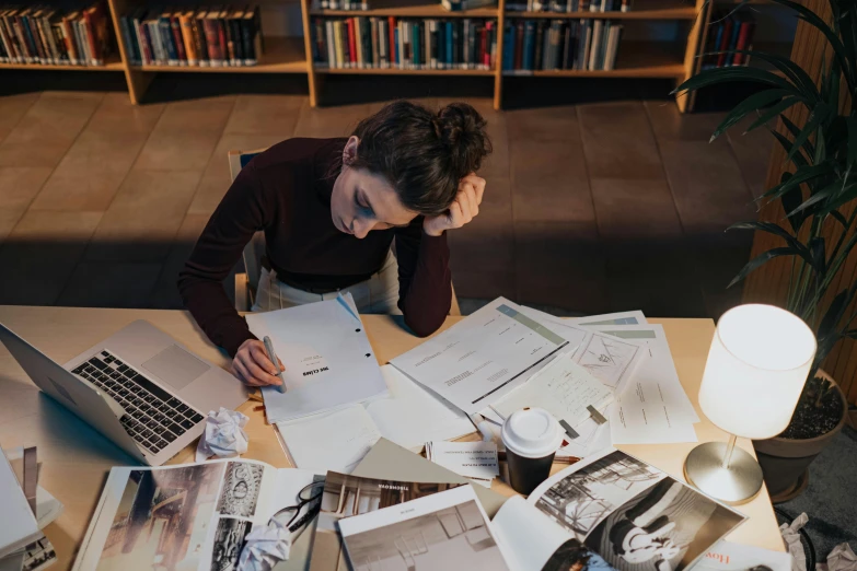 a woman sitting at a table in front of a laptop computer, by Julia Pishtar, pexels contest winner, academic art, piles of paperwork, sitting on a mocha-colored table, lachlan bailey, studious