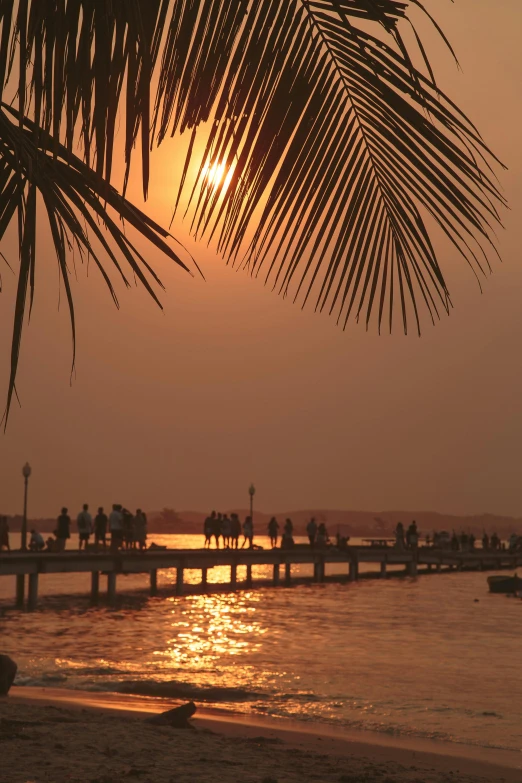 a group of people standing on top of a sandy beach, during a sunset, cambodia, near a jetty, islands