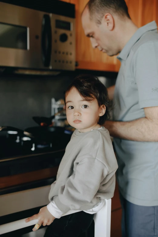 a man standing next to a little boy in a kitchen, pexels contest winner, looking serious, gif, bedhead, girl standing