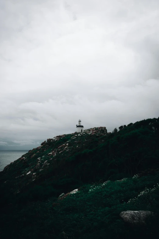 a lighthouse sitting on top of a lush green hillside, a picture, unsplash contest winner, romanticism, overcast gray skies, low quality photo, multiple stories, ominous photo