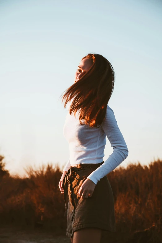 a woman standing in a field with her hair blowing in the wind, making the best smug smile, wearing tight simple clothes, 2019 trending photo, sunlit sky