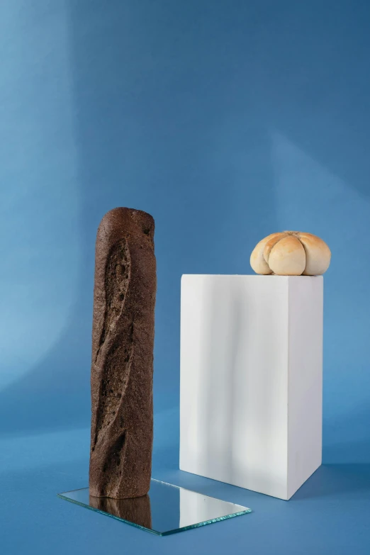 a piece of chocolate sitting on top of a table next to a piece of bread, an abstract sculpture, new sculpture, baking french baguette, studio product shot, large tall, pillar