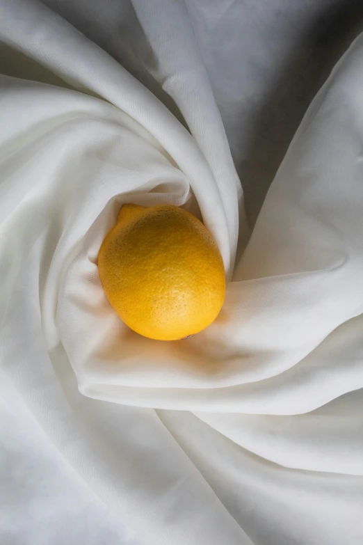 an orange sitting on top of a white cloth, yellow aureole, flowing silk sheets, wearing a lemon, lpoty