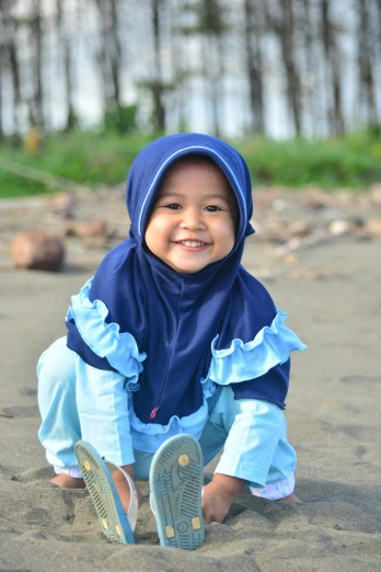 a small child sitting on top of a sandy beach, a picture, inspired by Nazmi Ziya Güran, hurufiyya, wearing a blue hoodie, shawl, high quality upload, modelling