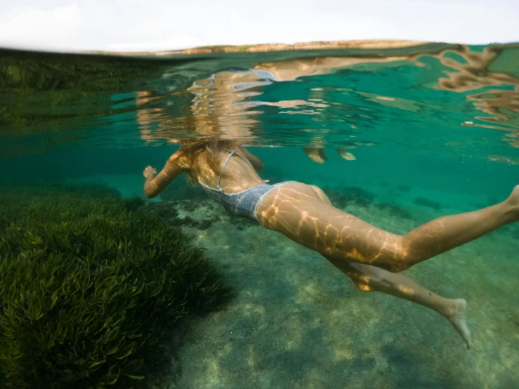 a woman in a bikini swims in the clear water, a picture, by Jessie Algie, unsplash contest winner, grass and water, covered in coral, slightly tanned, underlit