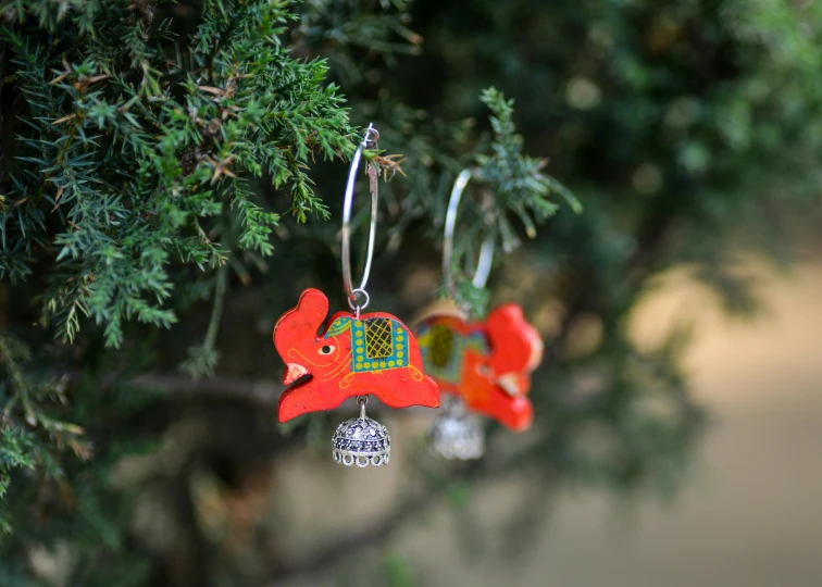 a pair of earrings hanging from a tree, unsplash, folk art, an elephant king, wooden decoration, vibrant red and green colours, side - view