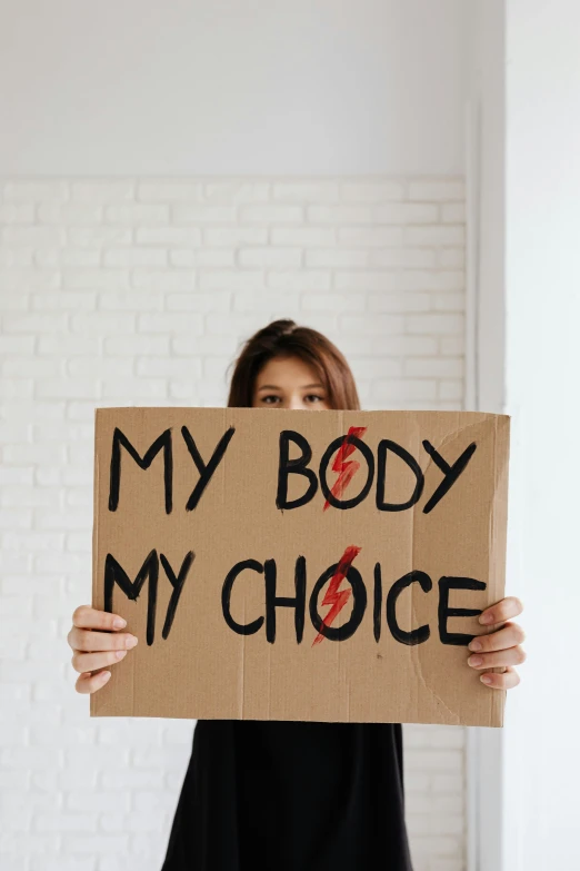 a woman holding a sign that says my body is my choice, by Julia Pishtar, trending on pexels, organs, biological, bodyhorror, cardboard