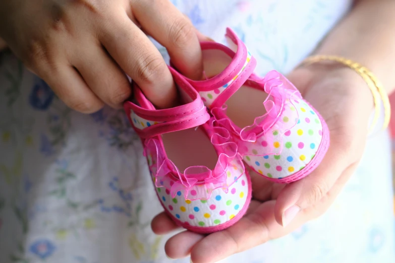 a close up of a person holding a pair of baby shoes, pink shoes, multi colour, polkadots, image