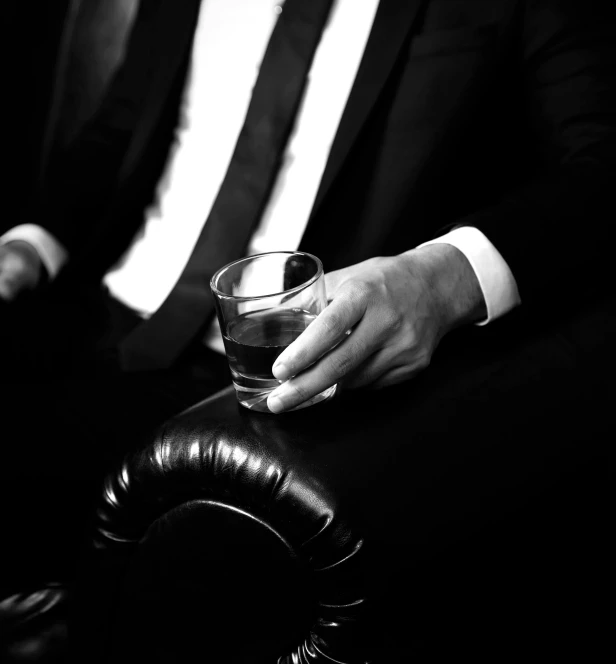a man in a suit holding a glass of alcohol, a black and white photo, by Emma Andijewska, purism, dr dre, mafia, lounge, new album cover