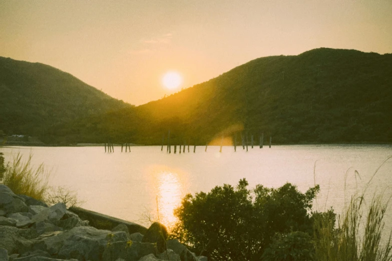 the sun is setting over a body of water, a picture, inspired by Elsa Bleda, unsplash contest winner, australian tonalism, taken with polaroid kodak portra, river and trees and hills, near a jetty, grainy vintage