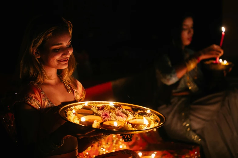 a woman holding a tray of food with lit candles, by Caroline Mytinger, pexels, hurufiyya, hindu ornaments, avatar image, partylights, ground level shot