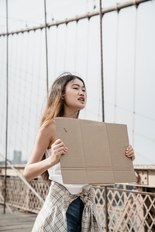 a woman standing on a bridge holding a cardboard box, pexels contest winner, slightly tanned, asian features, nyc, panels