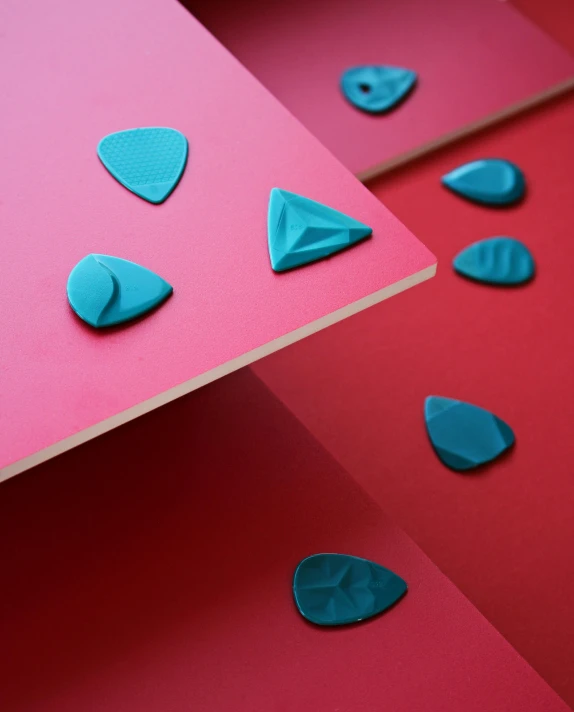 a couple of pieces of paper sitting on top of a table, inspired by Lucio Fontana, interactive art, turquoise and venetian red, polymer clay, studs, detail shot