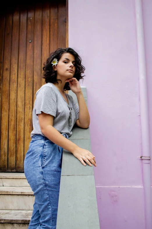 a woman leaning against a wall with a skateboard, an album cover, pexels contest winner, (dark shorter curly hair), fair olive skin, violet coloured t-shirt, wearing a linen shirt