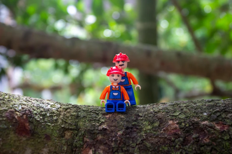 a couple of figurines sitting on top of a tree branch, inspired by Mario Comensoli, unsplash, wearing plumber uniform, woodland setting, lego, portrait mode photo