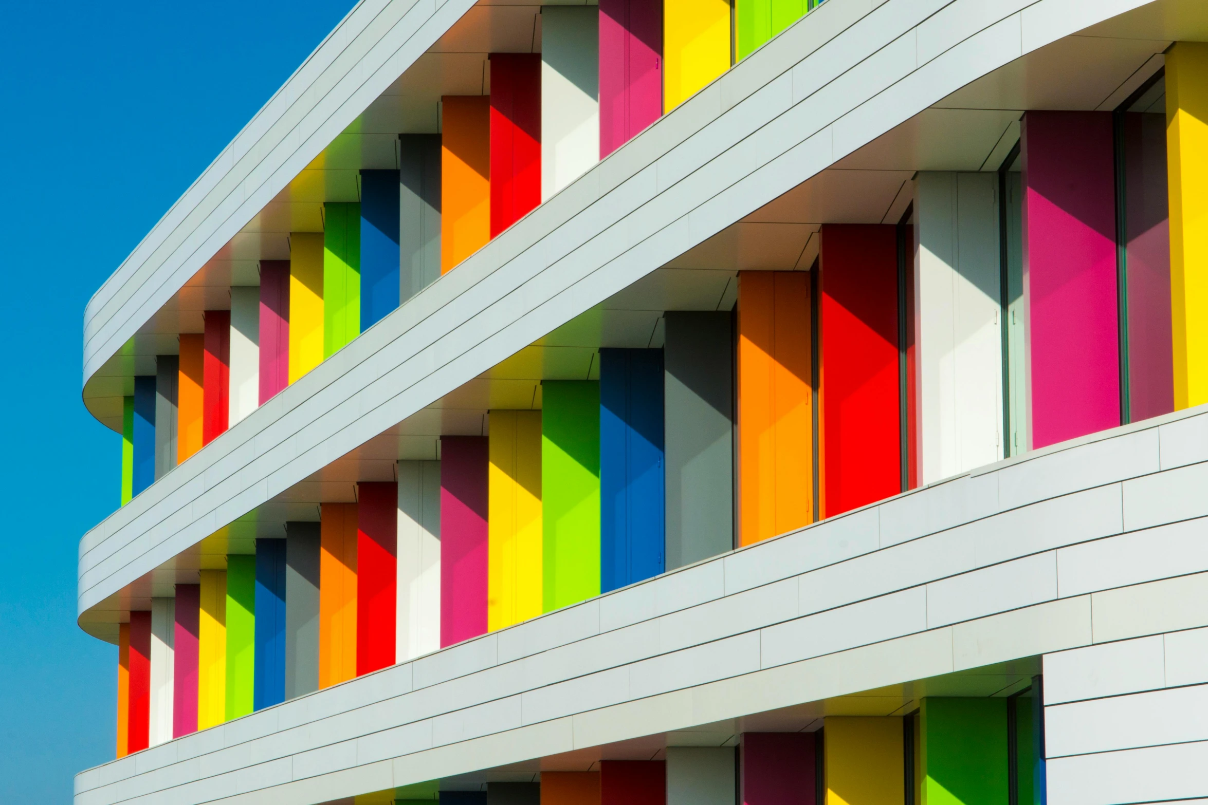 a multicolored building with a blue sky in the background, inspired by Bauhaus, unsplash, rainbow accents, shutters, schools, dezeen