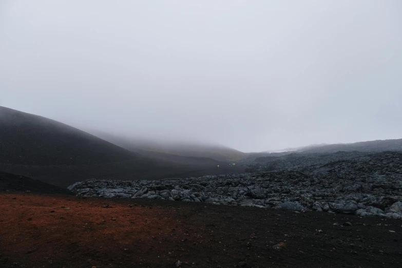 a person standing on top of a mountain on a foggy day, by Hallsteinn Sigurðsson, hurufiyya, body with black and red lava, moonscape, ground - level medium shot, high-quality photo