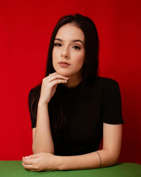 a woman sitting at a table in front of a red wall, trending on pexels, hailee steinfeld, plain background, portrait image, red on black