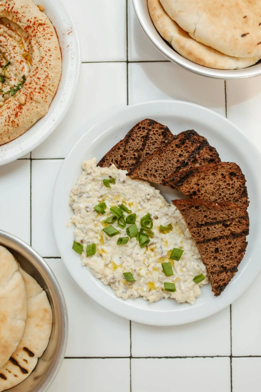 a table topped with plates of food and pita bread, dau-al-set, big oatmeal, sleek white, jen atkin, close up image