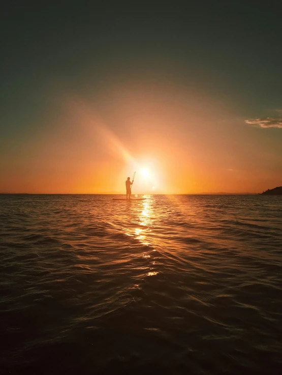 a person standing on a surfboard in the ocean at sunset, in the water