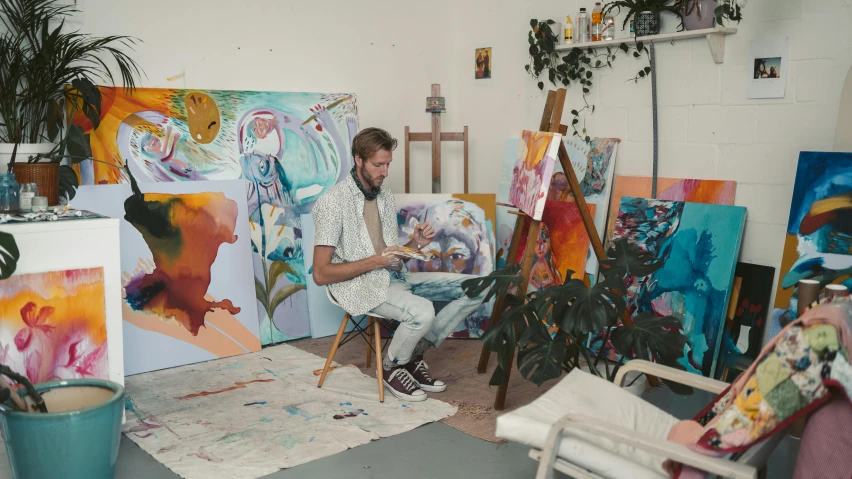 a man sitting in a chair in front of a painting, inspired by James Jean, pexels contest winner, stands at a his easel, liam brazier and nielly, in a white boho style studio, lachlan bailey