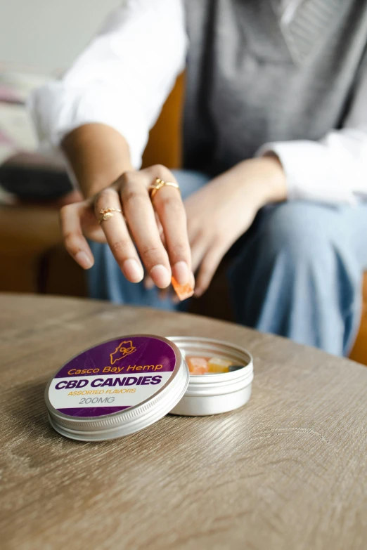 a close up of a person sitting at a table, holding a tin can, candy treatments, purple haze, official product image