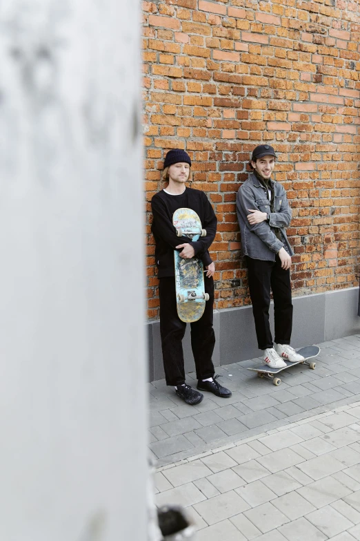 a group of people standing next to a brick wall, skateboard, petros and leonid, wearing black clothes, portrait image