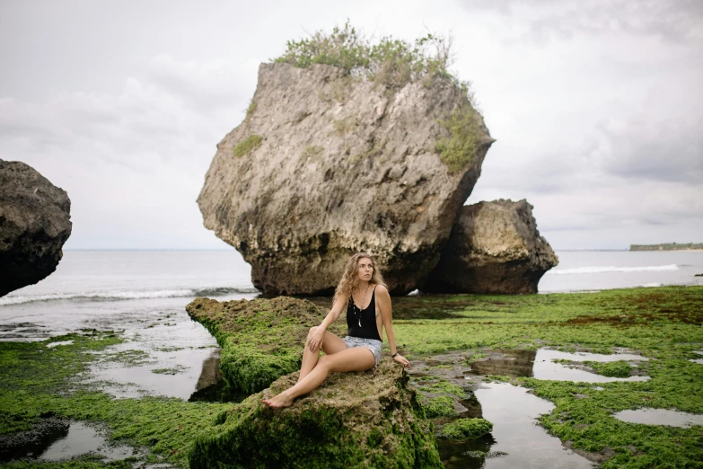 a woman sitting on a rock in front of a body of water, bali, the body of ronda rousey, medium format, lachlan bailey