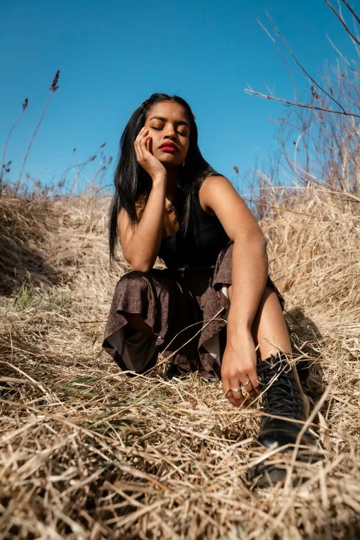 a woman sitting in a field talking on a cell phone, an album cover, trending on pexels, renaissance, indian girl with brown skin, menacing pose, dry grass, high quality photo