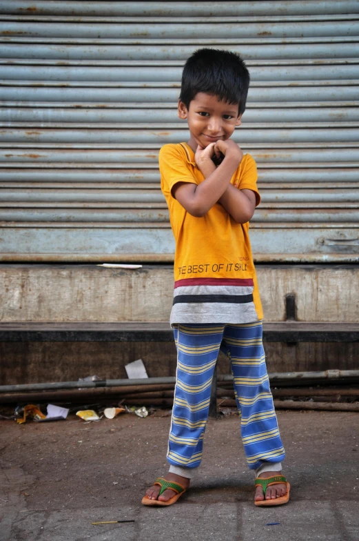 a young boy standing in front of a garage door, pexels contest winner, happening, on an indian street, stripey pants, cleft chin, compassion