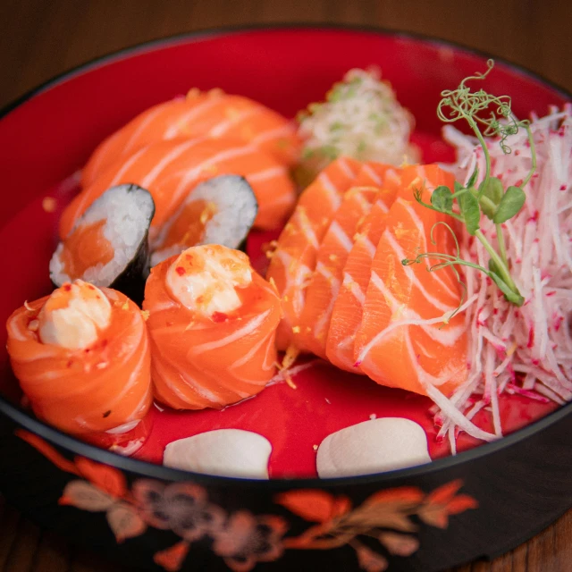 a red bowl filled with sushi on top of a wooden table, offering a plate of food, salmon, prawn, daily specials