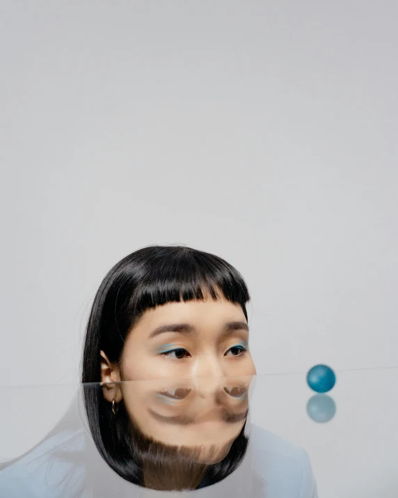 a woman with a fake smile on her face, an album cover, inspired by Gao Cen, trending on unsplash, surrealism, blue transparent jelly, half asian, sphere, looking into a mirror