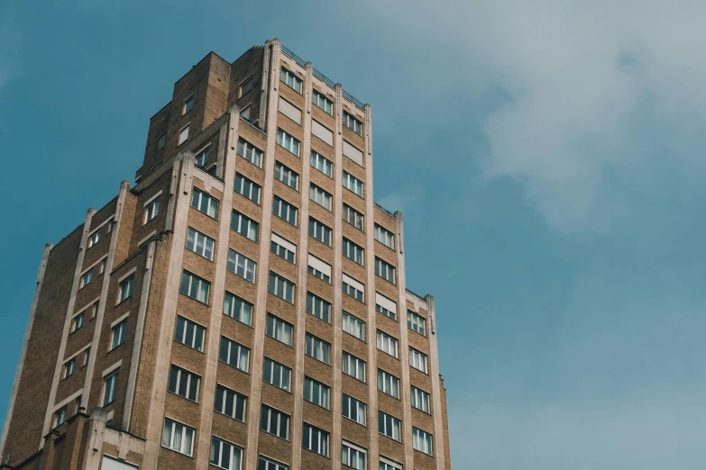 a tall brown building with lots of windows, unsplash, brutalism, 1940s photo, stood on top of a sky scraper, low dutch angle, art deco style