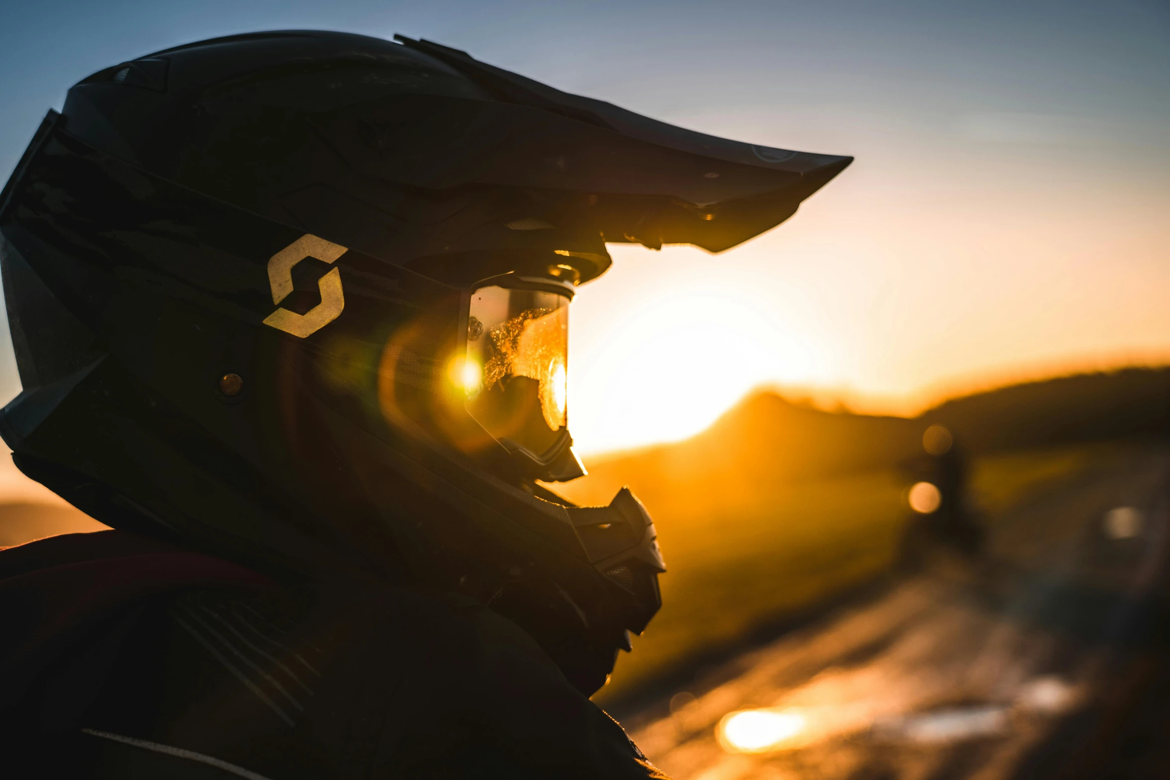 a person wearing a helmet with the sun setting in the background, a picture, by Sebastian Spreng, off - road, profile image, sharp details, reflective visor