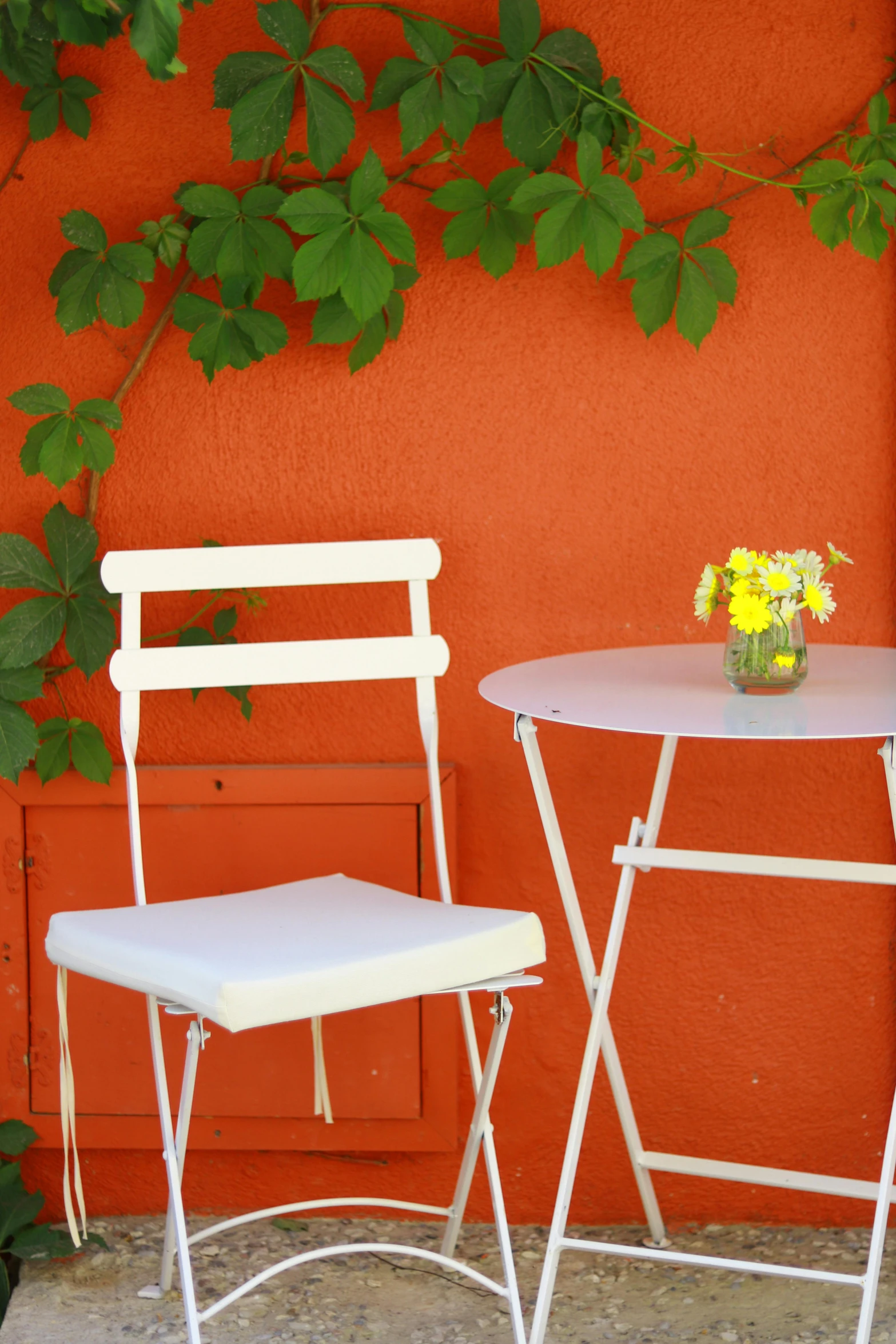 two chairs and a table in front of an orange wall, garden setting, complimentary colours, white colors, tea