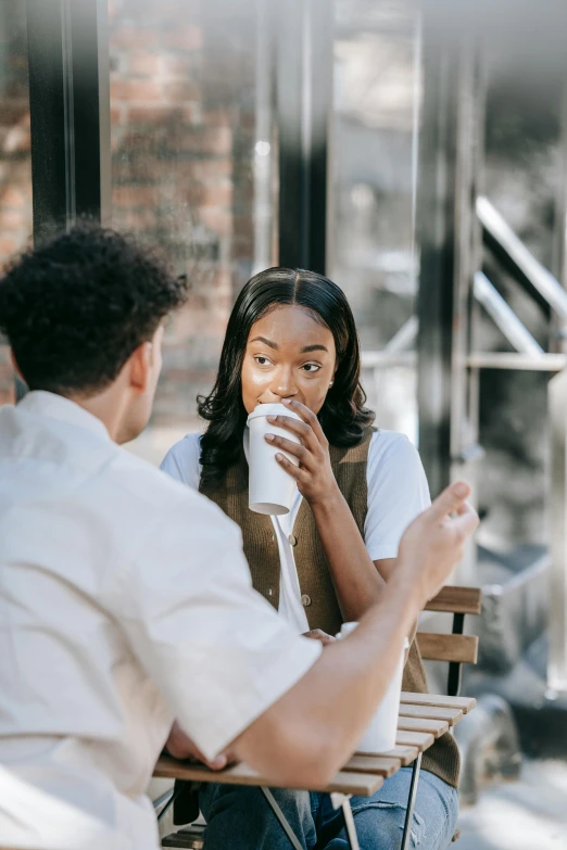 a man and woman sitting at a table drinking coffee, trending on pexels, happening, mixed race, realistic »