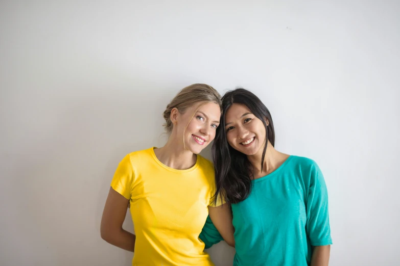 a couple of women standing next to each other, pexels contest winner, wearing a modern yellow tshirt, diverse colors, half asian, white bg