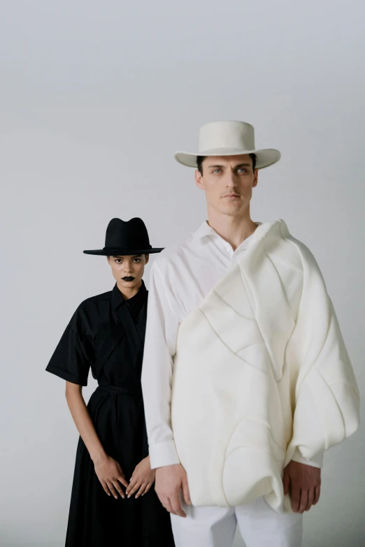 a man and a woman standing next to each other, inspired by Karl Buesgen, trending on unsplash, bauhaus, white hat, at a fashion shoot, white ribbon, in front of white back drop