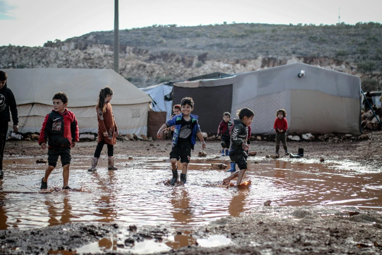 a group of children playing in a muddy field, by Daren Bader, trending on unsplash, hurufiyya, camps in the background, jordan, wet floors, cardboard