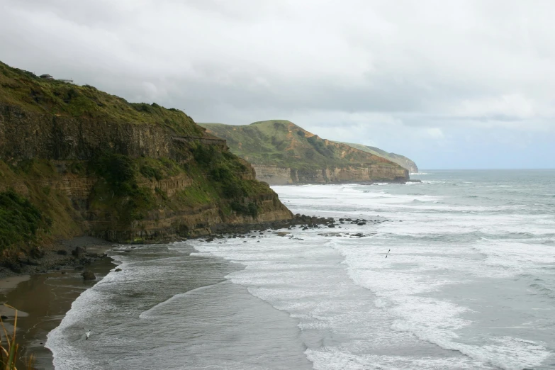 a large body of water next to a lush green hillside, by Peter Churcher, pexels contest winner, hurufiyya, stormy coast, slate, te pae, soft-sanded coastlines