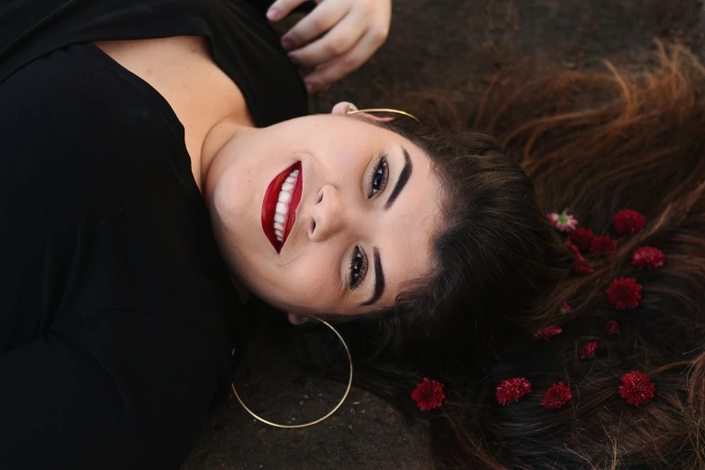 a woman laying on the ground with red flowers in her hair, pexels contest winner, cheeky smile with red lips, black lipstick, ariel perez, headshot profile picture