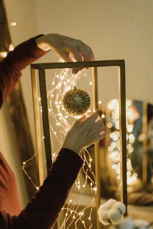 a woman placing a christmas ornament in a frame, pexels contest winner, warm lantern lighting, thin gold details, string lights, profile image