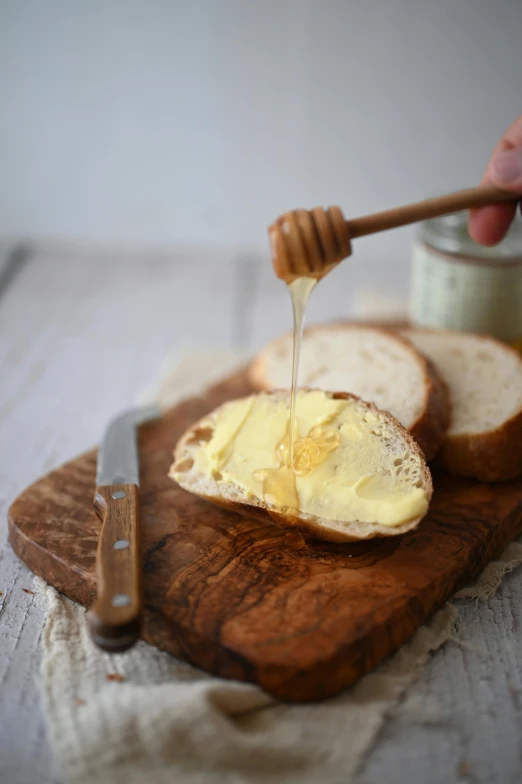 a wooden cutting board topped with slices of bread, by Sylvia Wishart, unsplash, hurufiyya, jar of honey, molten, cream, high quality photo