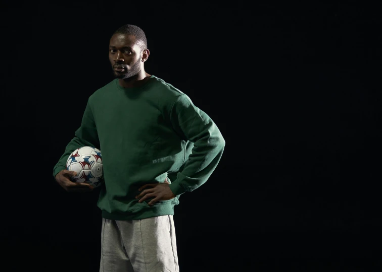 a man in a green shirt holding a soccer ball, by Paul Davis, cinematic still, black main color, medium format. soft light, wearing a track suit