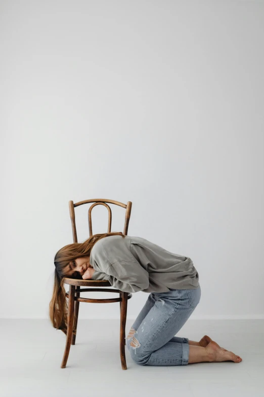 a woman sitting on top of a wooden chair, by Nina Hamnett, pexels contest winner, renaissance, face down, bending poses, plain background, facepalm